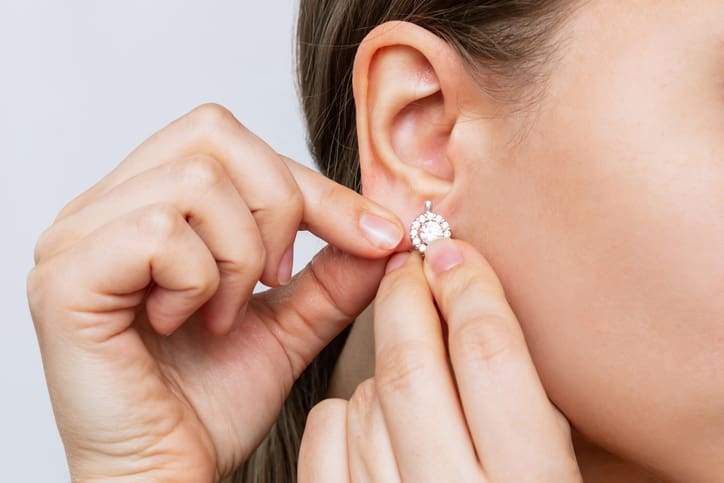 Cropped shot of a young woman wearing elegant diamond earrings on a gray background. Jewelry concept Medical Ear Piercing in New York, NY